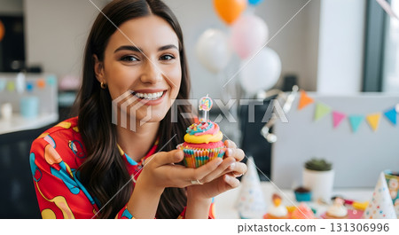 Cheerful woman holding a cupcake at a birthday office party. Cheerful woman holding a cupcake at a birthday office party. 131306996