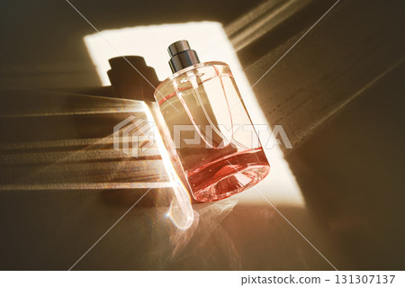 Pink perfume bottle on the light background in the rays of sun with highlights. 131307137