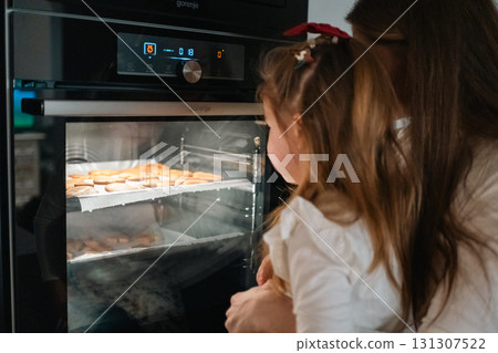 A child and caregiver enjoy watching cookies bake together in the warm oven, sharing a special moment 131307522