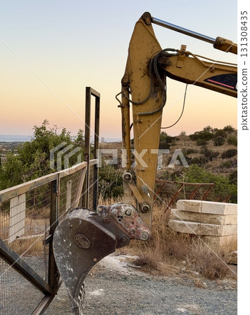 An excavator bucket propped up a metal gate. A crawler excavator stands at a construction site. Construction machinery and equipment. An excavator bucket propped up a metal gate. A crawler excavator stands at a construction site. Construction machinery and equipment. 131308435