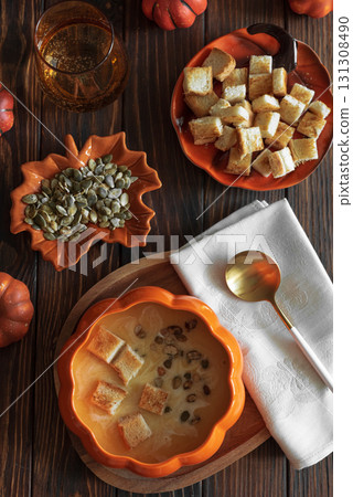 Creamy pumpkin soup with croutons and seeds, served in a pumpkin-shaped bowl on dark wooden table. Top view 131308490