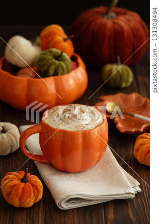 Cozy pumpkin latte in a pumpkin-shaped mug with whipped cream and spices, surrounded by autumn decor. Cozy pumpkin latte in a pumpkin-shaped mug with whipped cream and spices, surrounded by autumn decor. 131308494