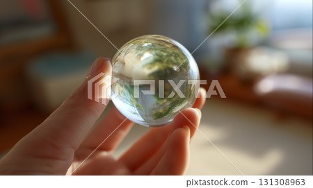 Hand holding a clear crystal lens ball reflecting the outdoors 131308963