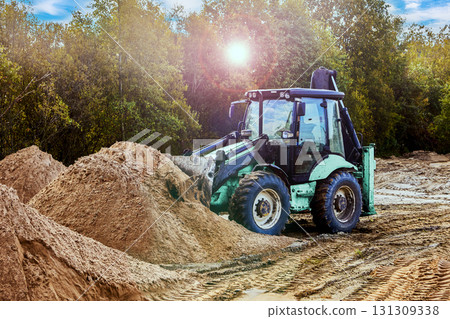 Backhoe loader distributes sand across construction site, creating uniform surface for upcoming development. Backhoe loader distributes sand across construction site, creating uniform surface for upcoming development. 131309338
