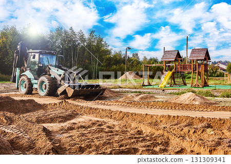 Backhoe loader levels sand surface by blade control and selective bucket drag to achieve required flatness for new base under playground equipment. Backhoe loader levels sand surface by blade control and selective bucket drag to achieve required flatness for new base under playground equipment. 131309341