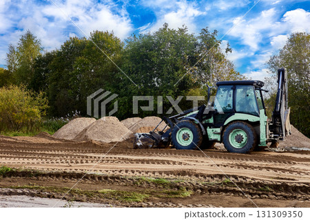 Front end loader performs finish grading by precisely redistributing loose sand layer and removing minor surface irregularities for optimal site compaction. Front end loader performs finish grading by precisely redistributing loose sand layer and removing minor surface irregularities for optimal site compaction. 131309350