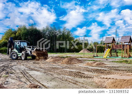 Loader pushes piles of sand across a flat construction site near wooden playground structures. Loader pushes piles of sand across a flat construction site near wooden playground structures. 131309352