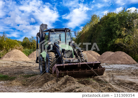 Wheel loader performs earthmoving work with sand piles visible on construction site. Wheel loader performs earthmoving work with sand piles visible on construction site. 131309354