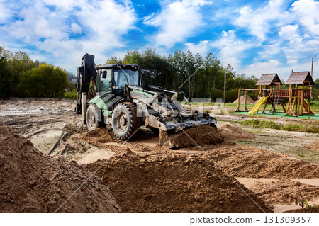 Wheel loader performs construction work with sand piles located on site near playground area. Wheel loader performs construction work with sand piles located on site near playground area. 131309357