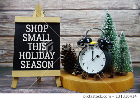 Thank You For Supporting Local written on easel with vintage alarm clock, pinecones, and miniature Christmas trees Thank You For Supporting Local written on easel with vintage alarm clock, pinecones, and miniature Christmas trees 131310414