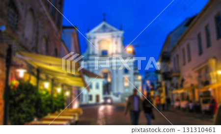 Evening city landscape, city street with lights and passers-by. Creative background with blur and bokeh for a poster, banner or screensaver. Evening city landscape, city street with lights and passers-by. Creative background with blur and bokeh for a poster, banner or screensaver. 131310461