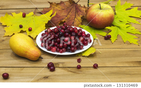 Autumn Still Life. Cranberries on a white plate, autumn leaves and an apple with a pear Autumn Still Life. Cranberries on a white plate, autumn leaves and an apple with a pear 131310469