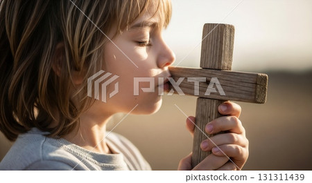 A child kisses a wooden cross gently. 131311439