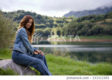 Young woman sitting on rock near scenic mountain lake Young woman sitting on rock near scenic mountain lake 131311991