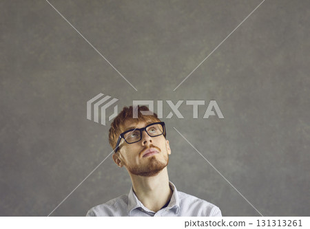 Thinking nerd man freelance programmer looking up over grey studio copy space Thinking nerd man freelance programmer looking up over grey studio copy space 131313261