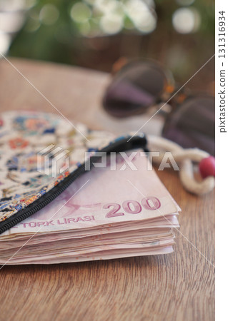 Currency and wallet on a wooden table with sunglasses nearby 131316934