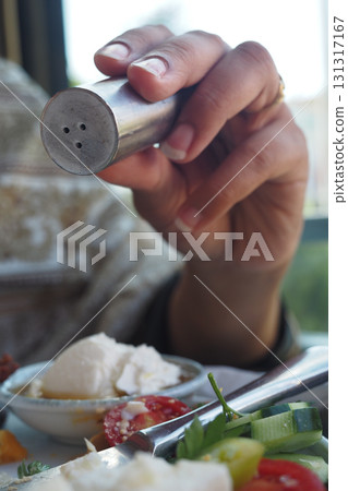 Hand holding a salt shaker over a plate of food 131317167