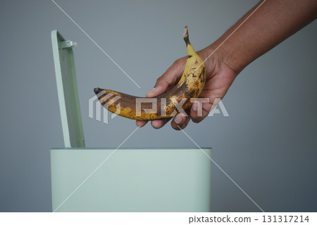 Hand discarding a ripe banana into a trash bin Hand discarding a ripe banana into a trash bin 131317214