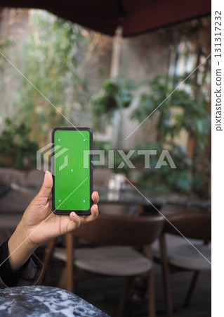 Smartphone held up in a cozy cafe with green screen display 131317232