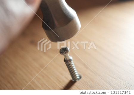Hammer striking metal screw on wooden surface Hammer striking metal screw on wooden surface 131317341
