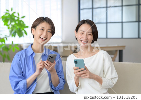 女人們並排坐在沙發上，看著自己的智慧型手機 131318203
