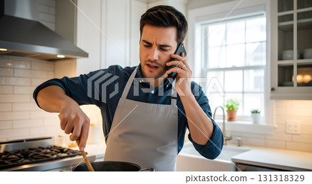 Man in apron stirs pot while on phone in bright kitchen 131318329
