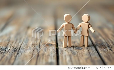 Two wooden figures holding hands on a wooden table, illustrating the bond of family and friendship in a serene environment Two wooden figures holding hands on a wooden table, illustrating the bond of family and friendship in a serene environment 131318956