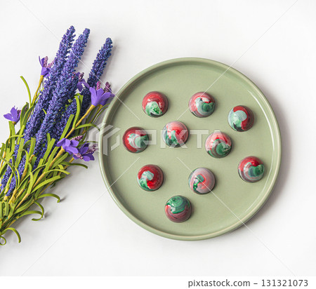 Collectible handmade tempered chocolate sweets with a glossy painted body on a round plate with blur elements. View from above 131321073