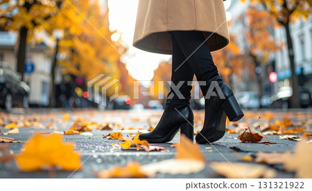 秋季，一位身穿駝色大衣和黑色踝靴的女子以低角度行走 131321922