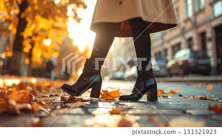 秋季，一位身穿駝色大衣和黑色踝靴的女子以低角度行走 131321923