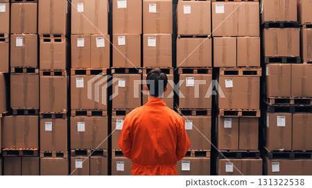 Warehouse worker in orange uniform facing stacked cardboard boxes 131322538