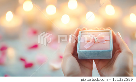 person holds small velvet jewelry box with ribbon, surrounded by candles 131322599