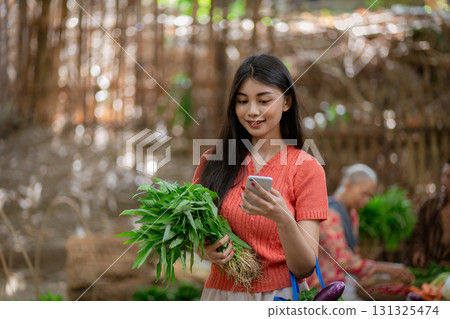 A Young Woman at an Outdoor Market Holding Fresh and Colorful Vegetables While Using Her Smartphone A Young Woman at an Outdoor Market Holding Fresh and Colorful Vegetables While Using Her Smartphone 131325474