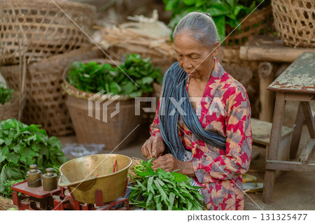 An Elderly Woman Engaged in the Preparation of Fresh Green Vegetables Within a Market Setting 131325477