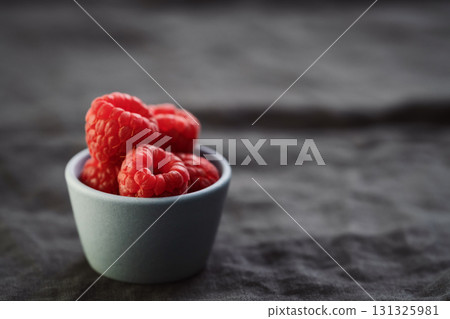 ripe raspberry in a small blue bowl on a linen background with copy space 131325981