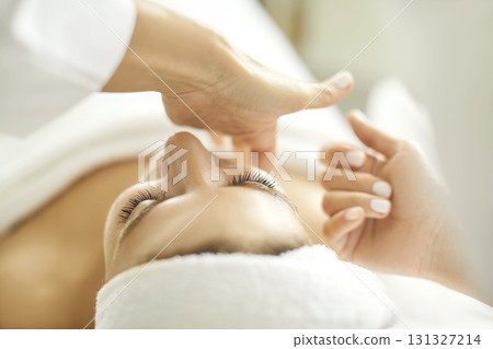 close up masseur hands making face relaxing massage to a young girl in beauty salon. close up masseur hands making face relaxing massage to a young girl in beauty salon. 131327214