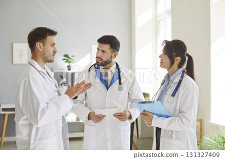 Three doctors engage in focused discussion in medical office during busy workday. 131327409