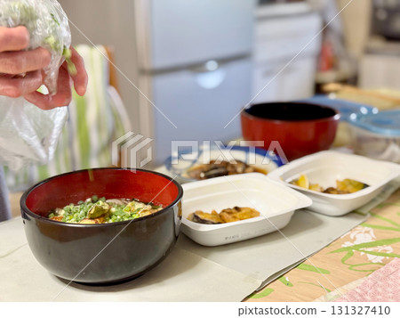 Elderly woman preparing a meal and holding a bag of green onions Elderly woman preparing a meal and holding a bag of green onions 131327410