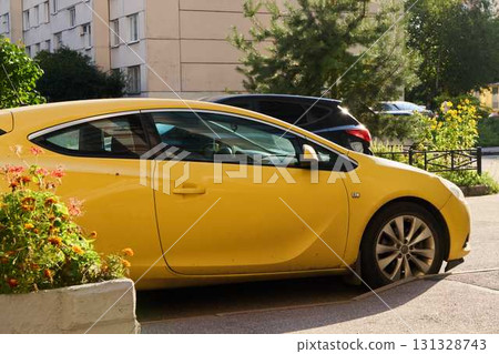 A bright yellow car is parked in a lively residential area, surrounded by several buildings 131328743