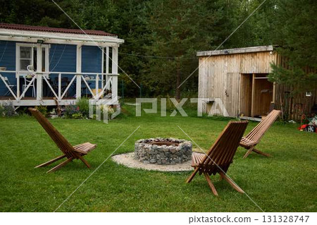Enjoy a cozy outdoor fire pit with comfortable chairs and a charming cabin in tranquility Enjoy a cozy outdoor fire pit with comfortable chairs and a charming cabin in tranquility 131328747