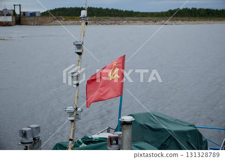 A red flag is visible on a boat that is docked at the waterfront, near the waters edge A red flag is visible on a boat that is docked at the waterfront, near the waters edge 131328789
