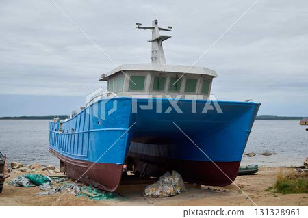 An Abandoned Blue Fishing Boat Resting on the Serene Shoreline, Evoking a Sense of Nostalgia 131328961