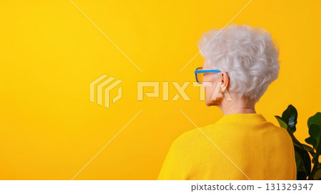 A thoughtful elderly woman with stylish white hair and glasses against a vibrant yellow backdrop A thoughtful elderly woman with stylish white hair and glasses against a vibrant yellow backdrop 131329347