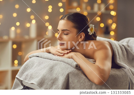 Young woman lying with closed eyes alone on massage couch in salon at wellness center. 131333085