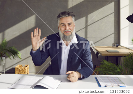 Senior businessman in suit attending online meeting, saying hello, and waving hand Senior businessman in suit attending online meeting, saying hello, and waving hand 131333092