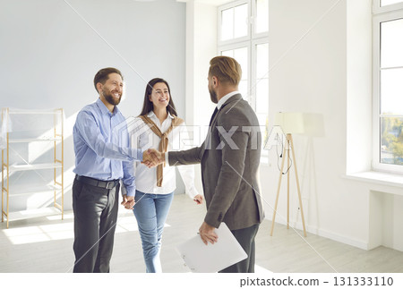 Happy young couple buying new house and exchanging handshake with real estate agent Happy young couple buying new house and exchanging handshake with real estate agent 131333110