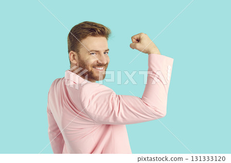 Smiling man celebrate victory with hand in fist demonstrating strength on blue background. Smiling man celebrate victory with hand in fist demonstrating strength on blue background. 131333120