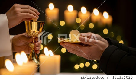 Priest hands holding golden chalice and communion wafer during holy eucharist ceremony with glowing candles and bokeh lights in background Priest hands holding golden chalice and communion wafer during holy eucharist ceremony with glowing candles and bokeh lights in background 131335026
