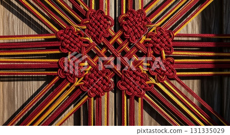 Traditional Chinese red and gold decorative knotwork with intricate endless knot pattern radiating from center on wooden background 131335029