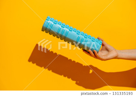 Hand holding a blue foam roller against orange background hard shadow fitness recovery at home 131335193